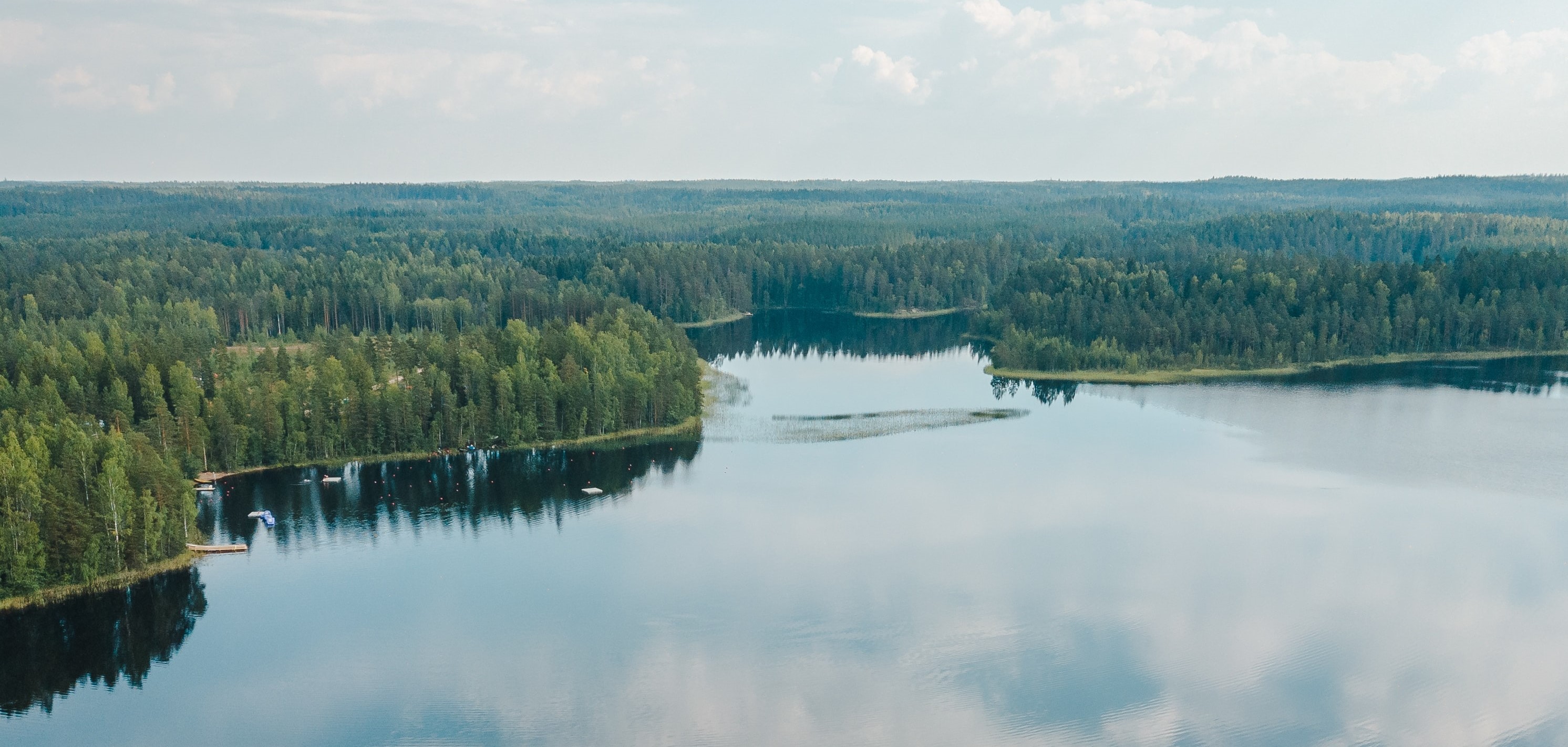 Tyyni järvi, jonka pinnasta heijastuu pilviä. Järven ympärillä kasvaa havumetsää.