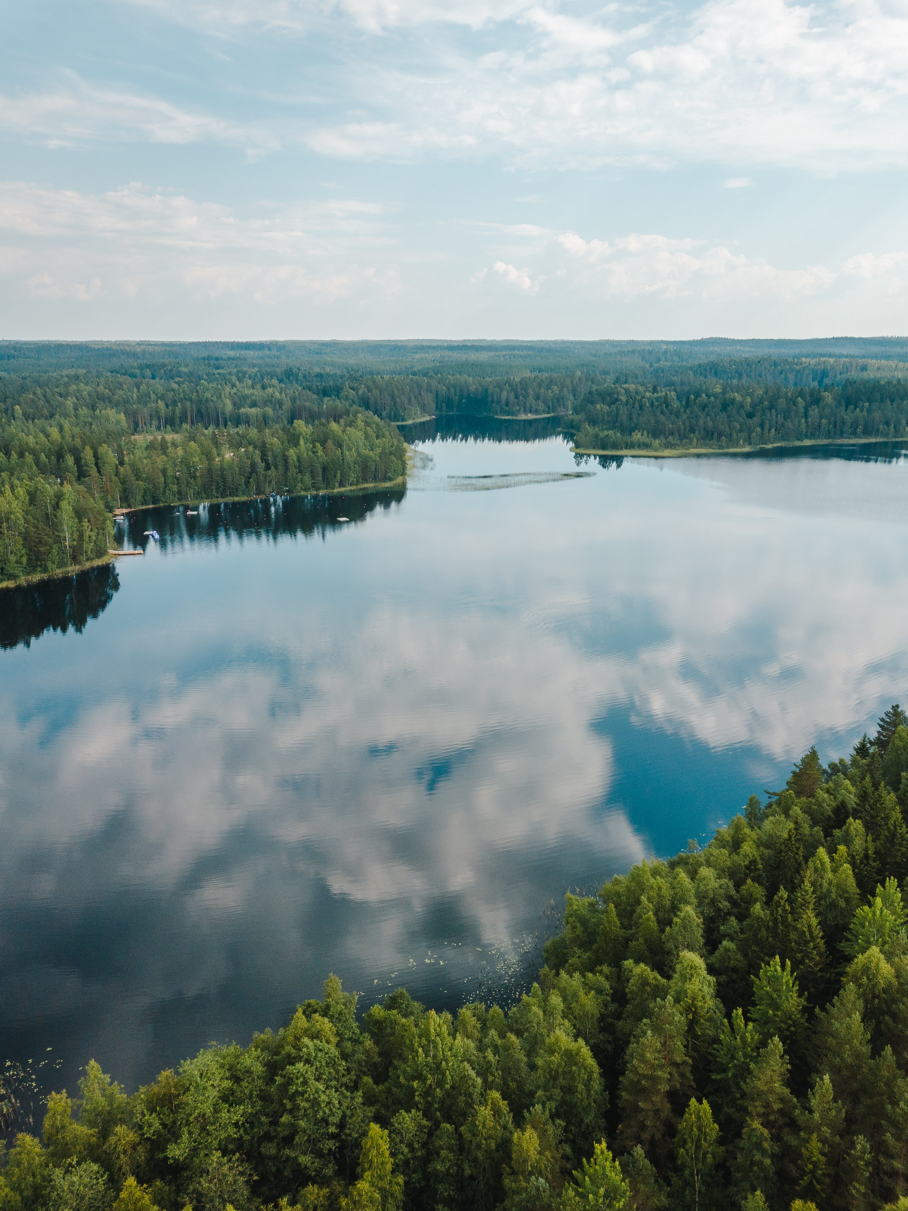 En blank sjö där molnen speglar sig i vattenytan. Runt sjön växer barrskog.