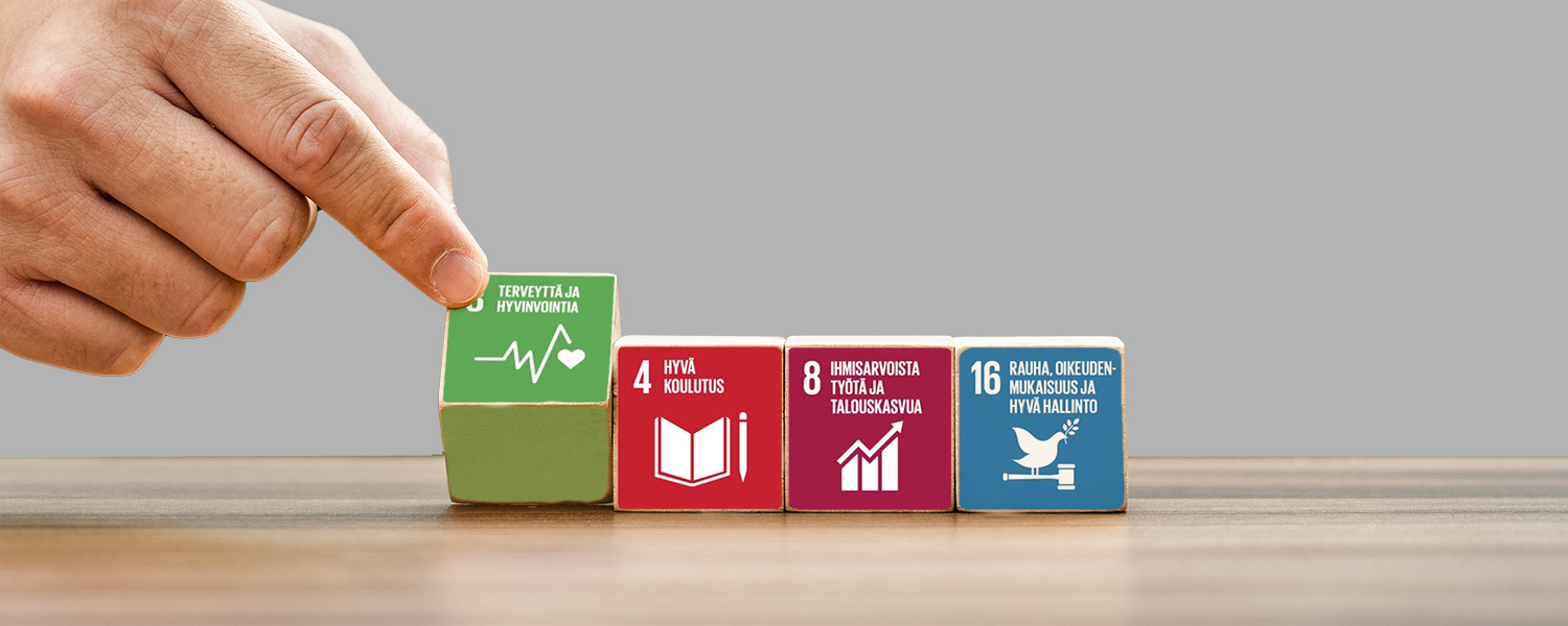 Neljä palikkaa pöydällä. Etusormi kääntää ympäri vasemmalla olevaa palikkaa. Palikoihin on merkitty YK:n tavoitteet 3, 4, 8 ja 16.