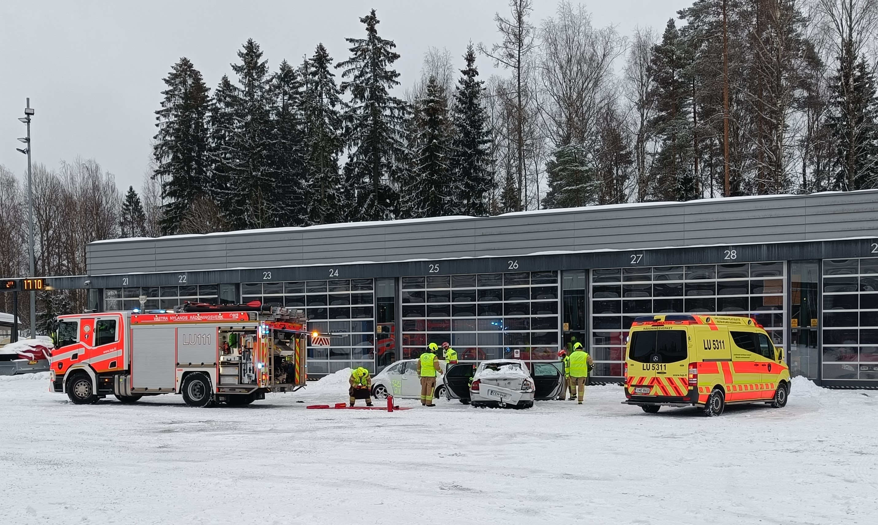 Krockad bil, räddningspersonal, brandbil och ambulans framför räddningsstationen.