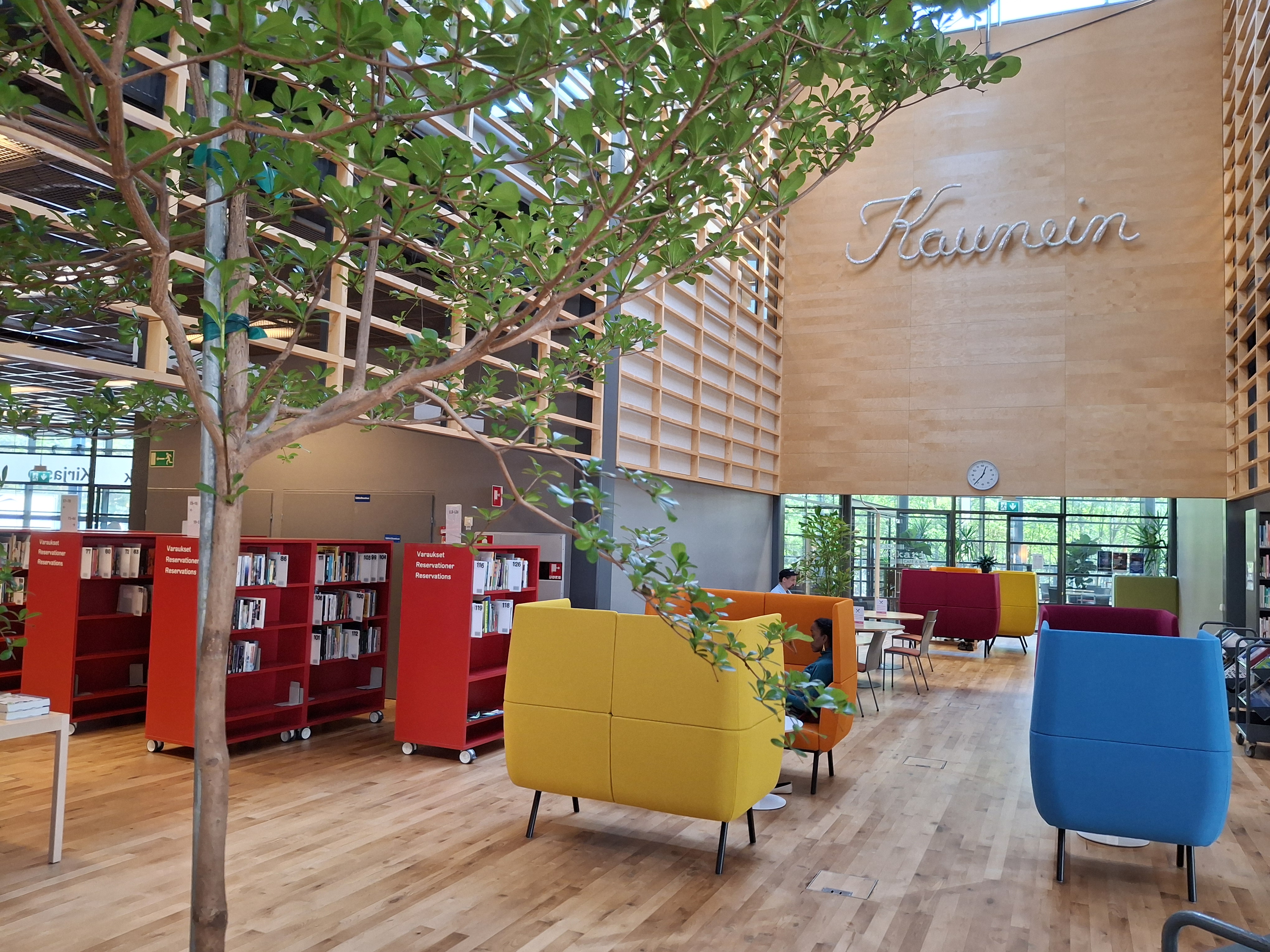 Vuosaari Library, lots of wood, green plants and colorful furniture and shelves.