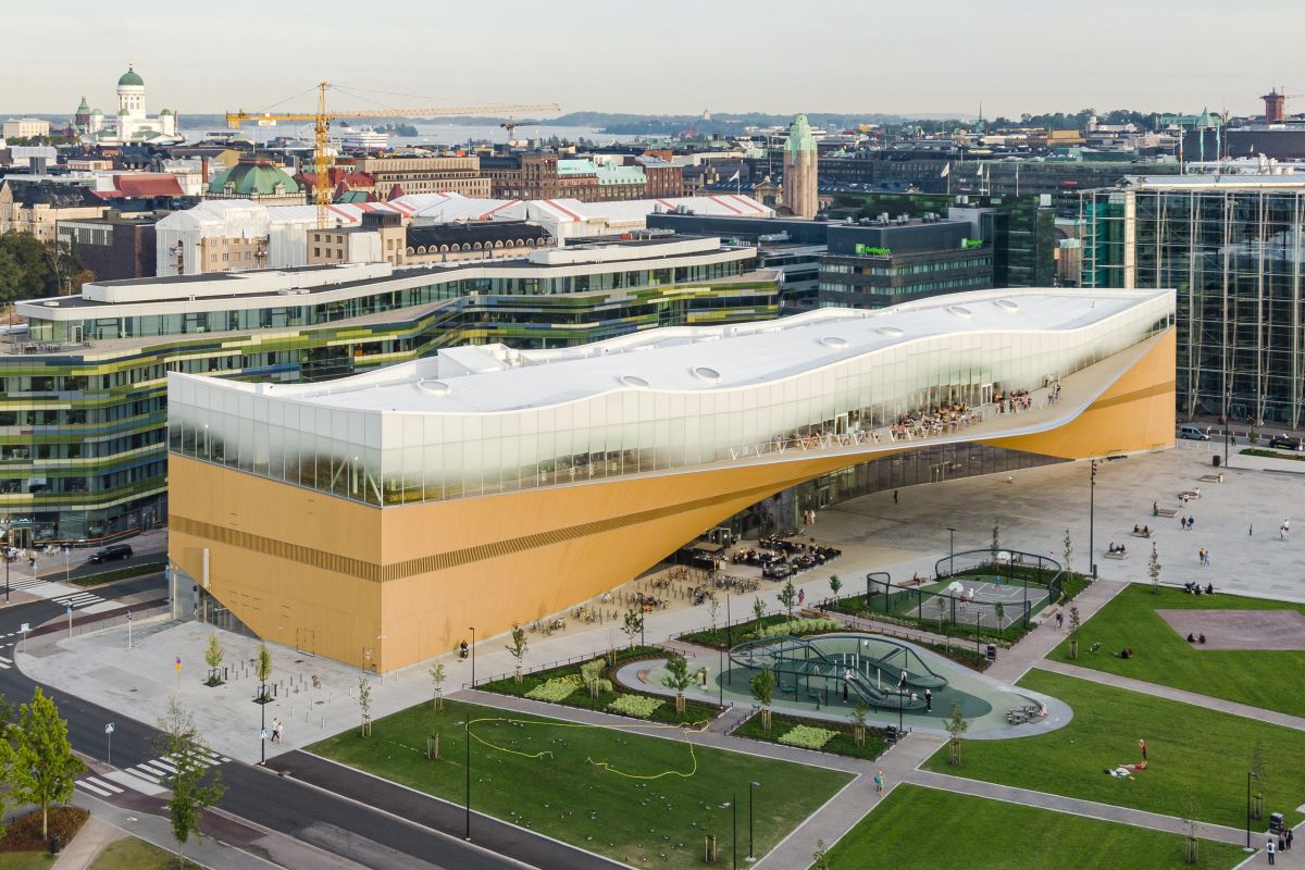 Aerial view of the Oodi Library: a long, undulating wooden building with a top glass floor painted with gradient white paint.